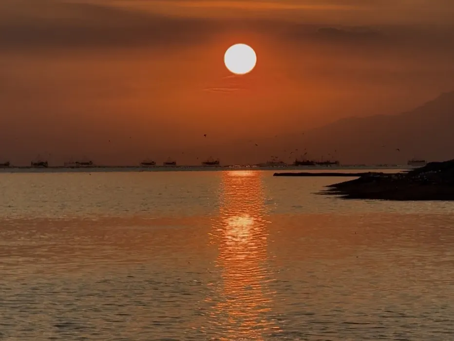 Sun setting over Manila Bay with fishing boats on the horizon
