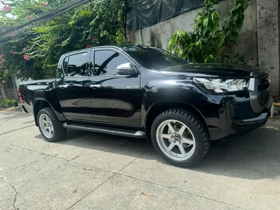 Black 2023 Toyota Hilux G double-cab pickup parked on a street beside a garden wall